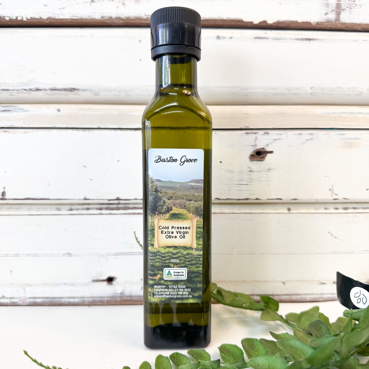 Bottle of BASTON GROVE Cold Pressed Extra Virgin Olive Oil with a scenic label on a wooden background