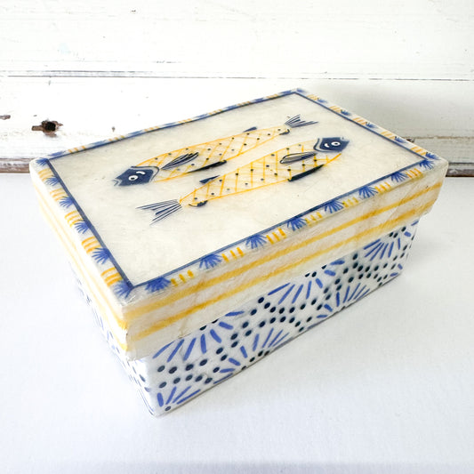 A hand-painted Capiz shell box with a design of fish and geometric patterns in blue, white, and yellow colors.