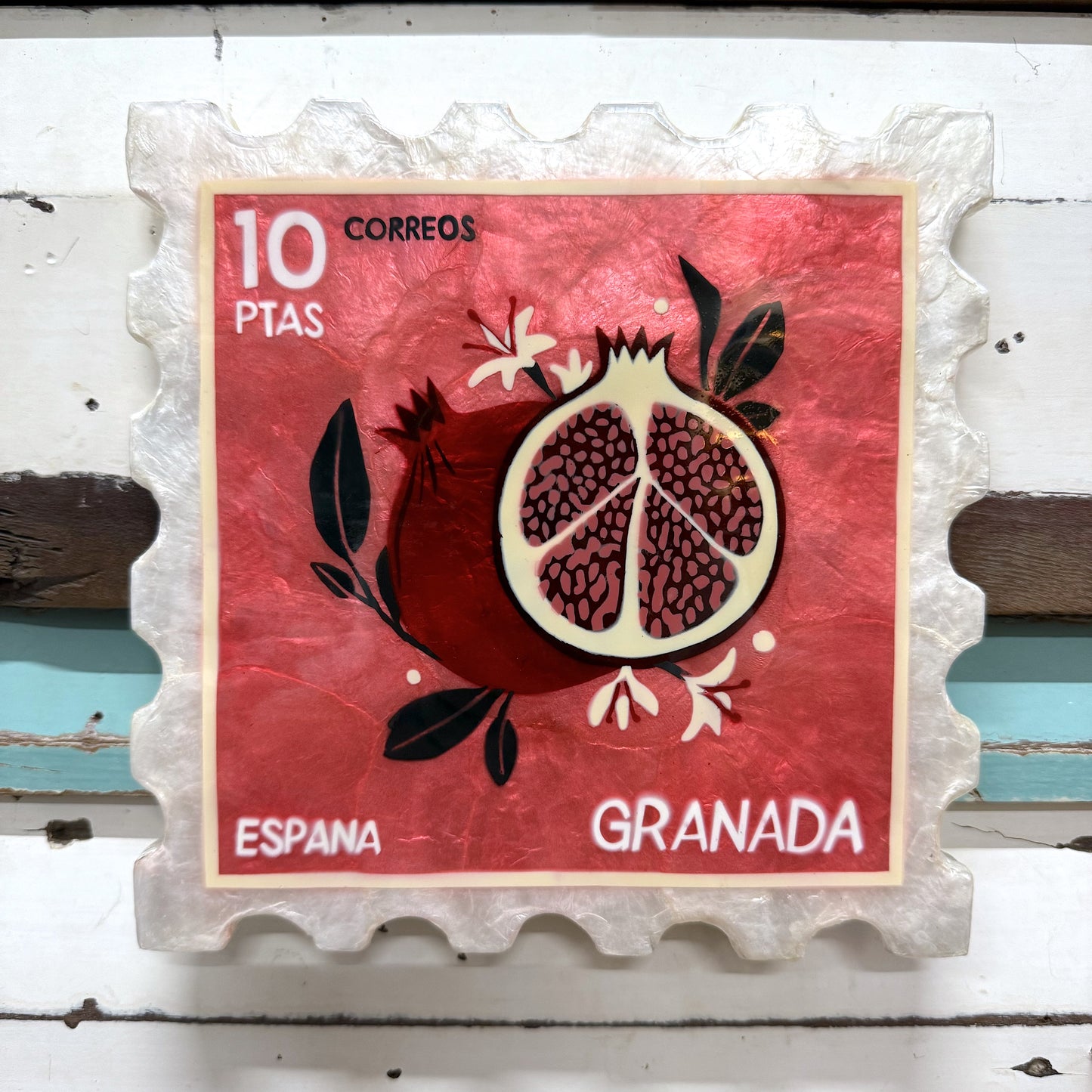 Jones & Co - Pomegranate Stamp-
A decorative plate with a pomegranate design, featuring the text '10 PTAS Espana Granada' on a red background, resembling a vintage postage stamp.