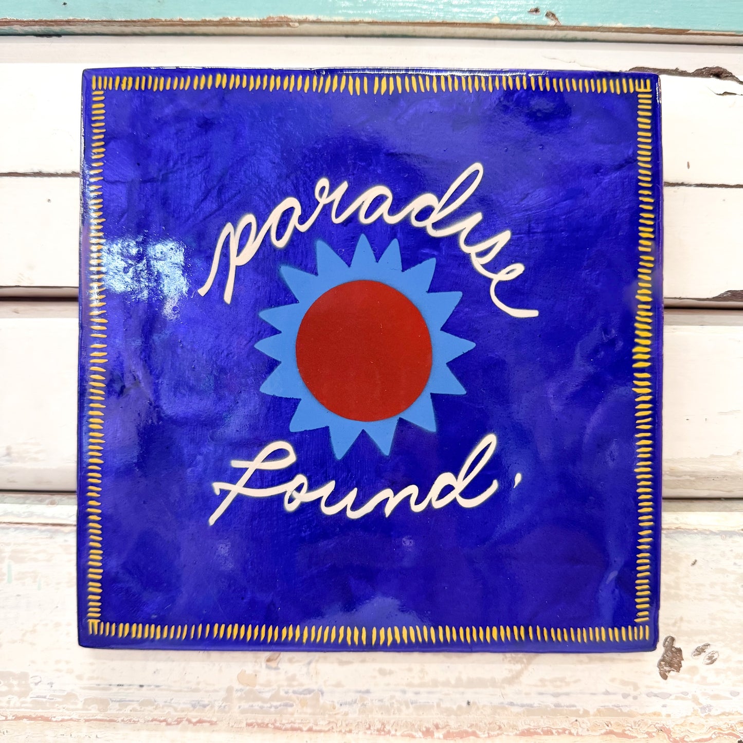 Decorative sign with 'paradise found' text and sun design on a blue background. Jones & Co - Superette Paradise Blue Tile