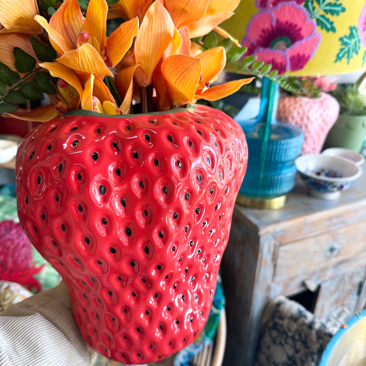 Kip&Co Strawberry Vase - Red strawberry-shaped vase with black pips & filled with green leaves and orange fruits.