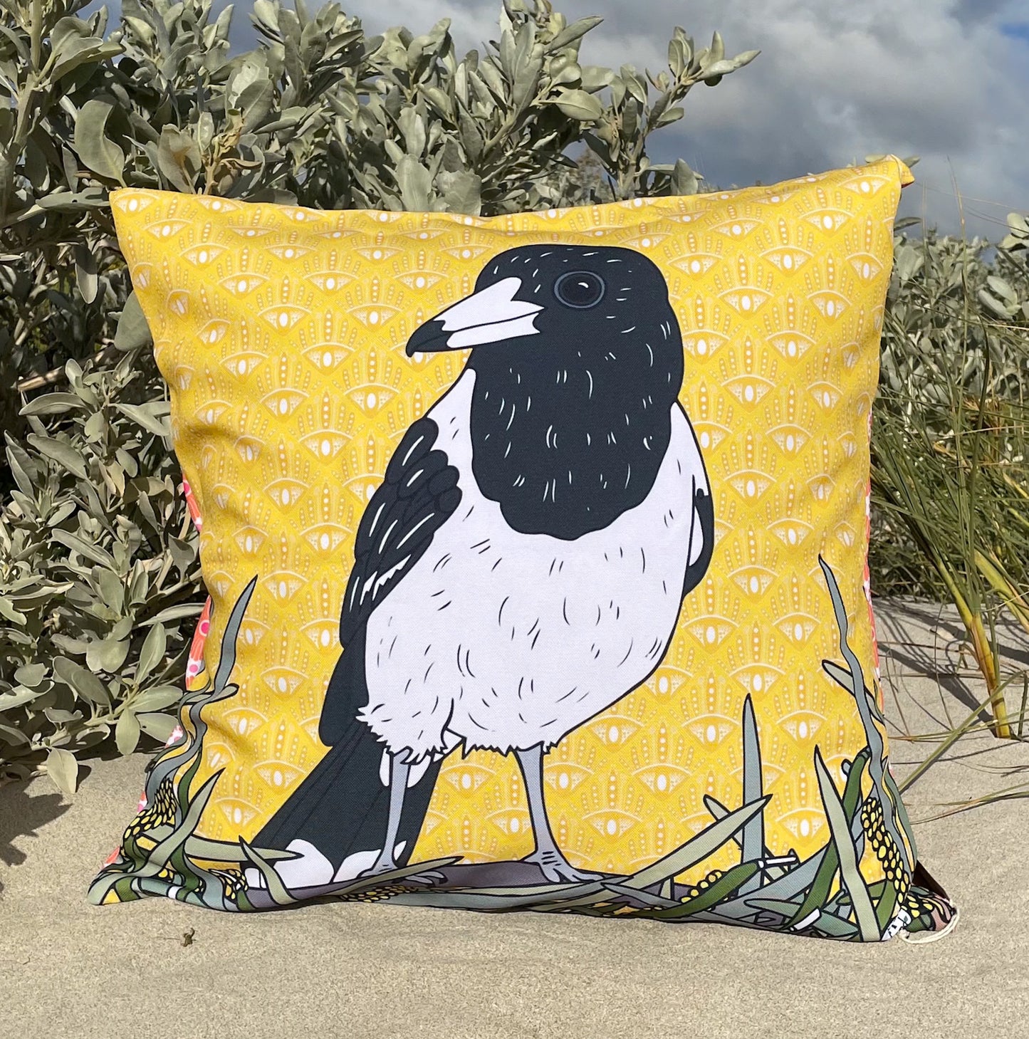 LOST AND FOUND ART CO Butcher Bird 60cm Cushion. Pillow with a magpie design on a yellow background, placed outdoors.