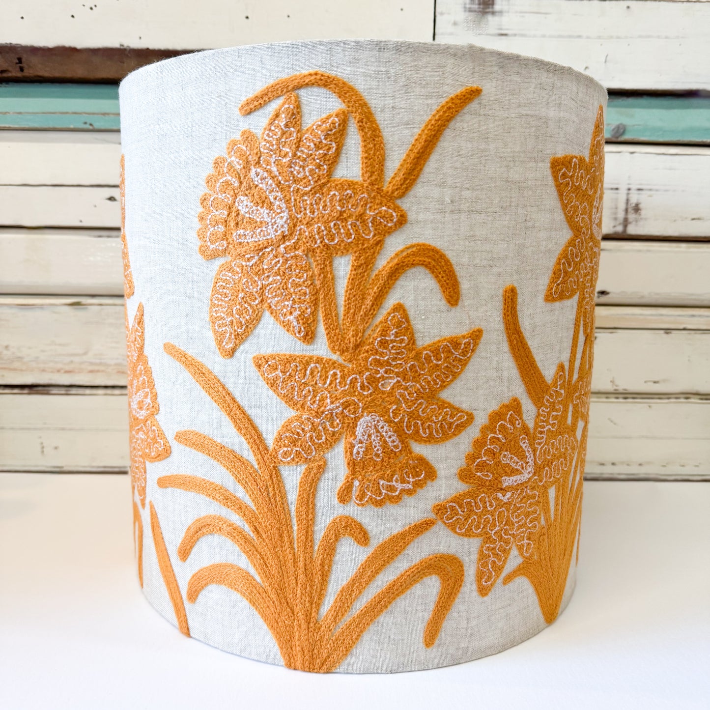 Decorative cylindrical lamp shade with orange floral daffodil stitched patterns on linen