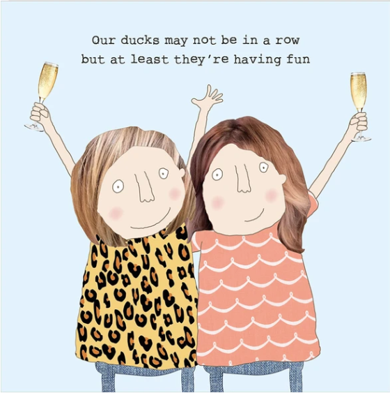 A whimsical illustrated greeting card or print featuring two cartoon girls holding champagne glasses, with the text 'Our ducks may not be in a row but at least they're having fun' on a light blue background.
