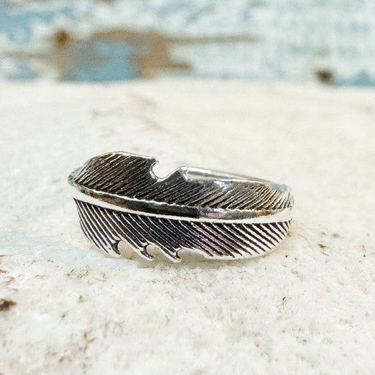 The Brightside Store - Feather Toe Ring Silver feather-shaped ring on a textured surface