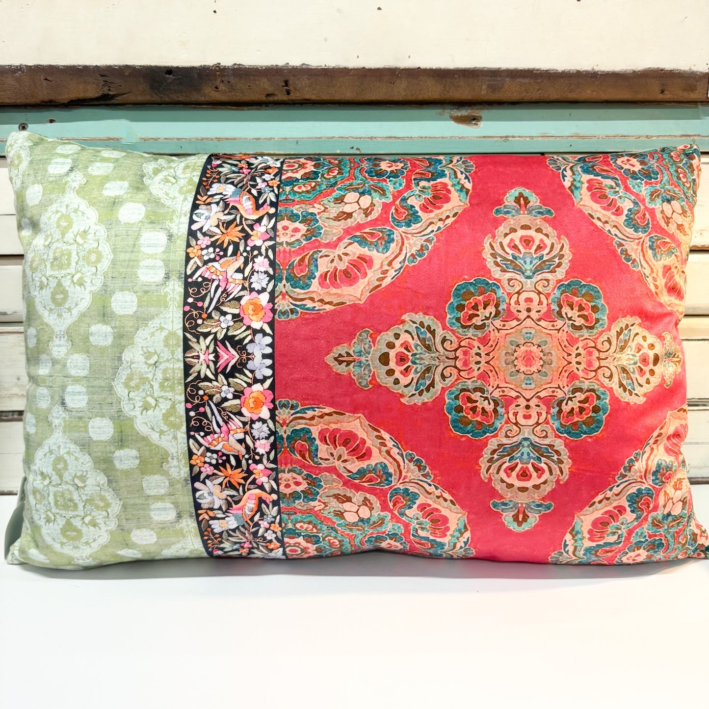 A rectangular decorative throw pillow with a multi-panel fabric design, featuring a red central panel with a teal and gold damask pattern, a green left panel with white floral motifs, and a narrow black floral border stripe.