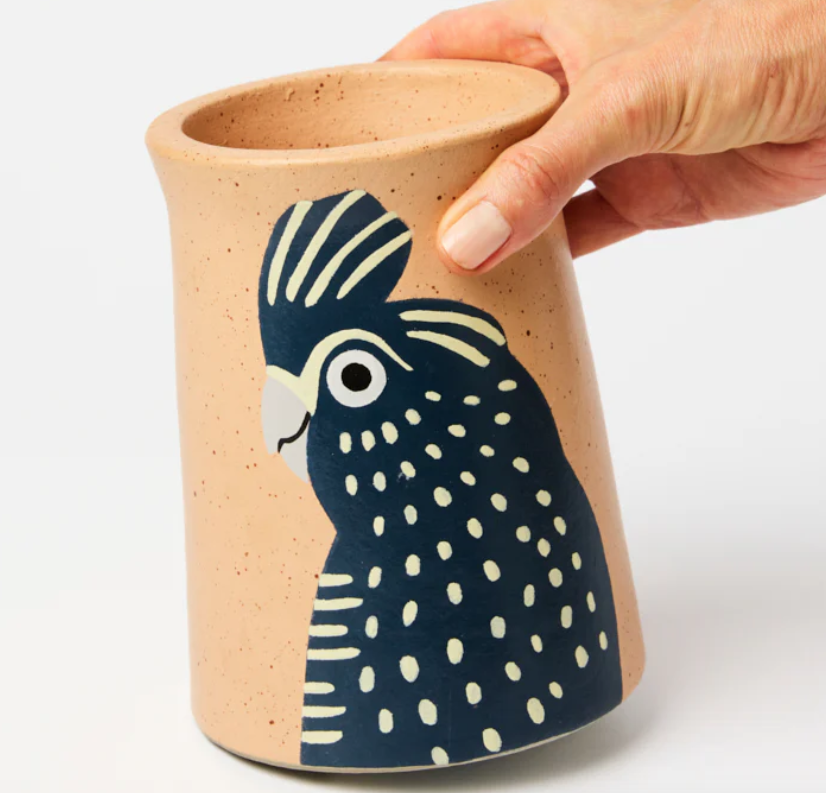 Ceramic vase with a black cockatoo design held by a hand on a white background
