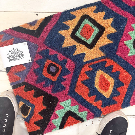 Colourful geometric-patterned coir doormat with 'Anna Chandler Design' label.