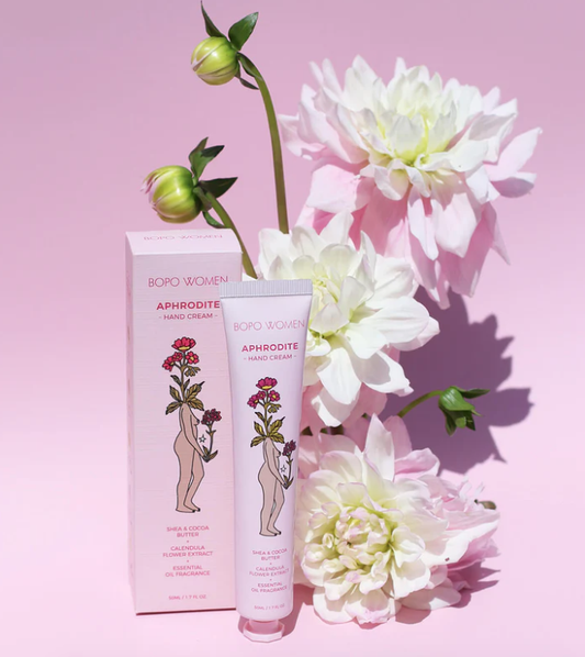 Bopo Women's Aphrodite hand cream with packaging on a pink background with flowers.