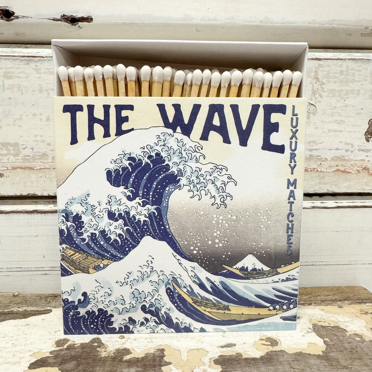 A box of luxury matches featuring a vintage-style print of 'The Wave at Kanagawa' on the front. The open box reveals wooden matches with white tips. 