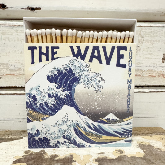 A box of luxury matches featuring a vintage-style print of 'The Wave at Kanagawa' on the front. The open box reveals wooden matches with white tips. 