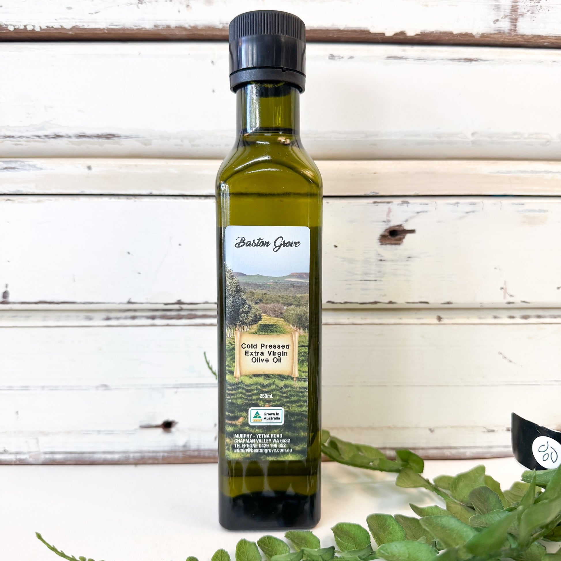Bottle of BASTON GROVE Cold Pressed Extra Virgin Olive Oil with a scenic label on a wooden background