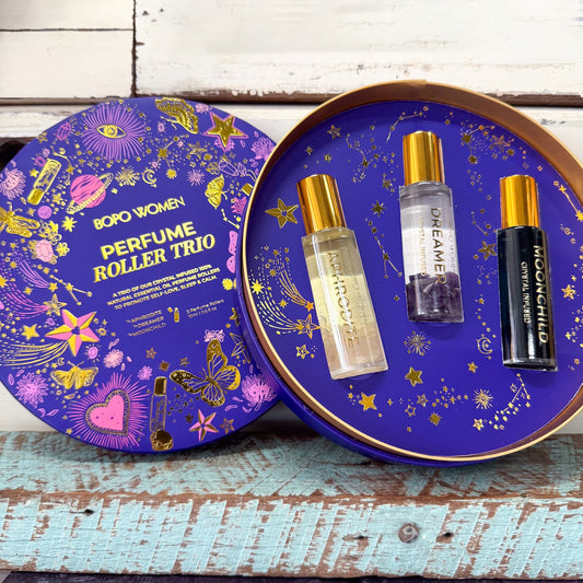 Boro Women Perfume Roller Trio gift set with three roller bottles displayed inside an open round tin next to its illustrated lid, set on a rustic wooden surface.