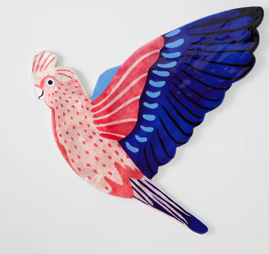 A hand-painted glossy Capiz shell wall tile in the shape of a bird with pink body and blue wings. Jones & Co - Aerial Galah