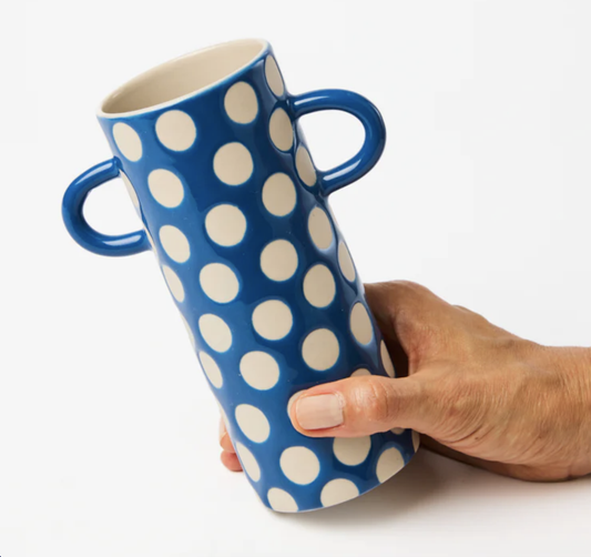 Blue mug with white polka dots held by a hand on a white background