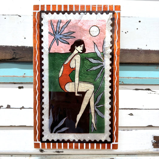 Jones & Co - Resort Dangle Tile; Artistic depiction of a woman in a red swimsuit sitting on a rock with plants and sky in the background, framed with decorative border.