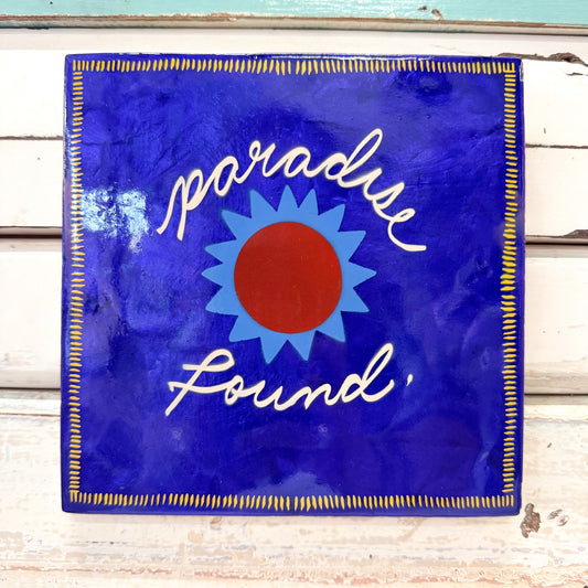 Decorative sign with 'paradise found' text and sun design on a blue background. Jones & Co - Superette Paradise Blue Tile