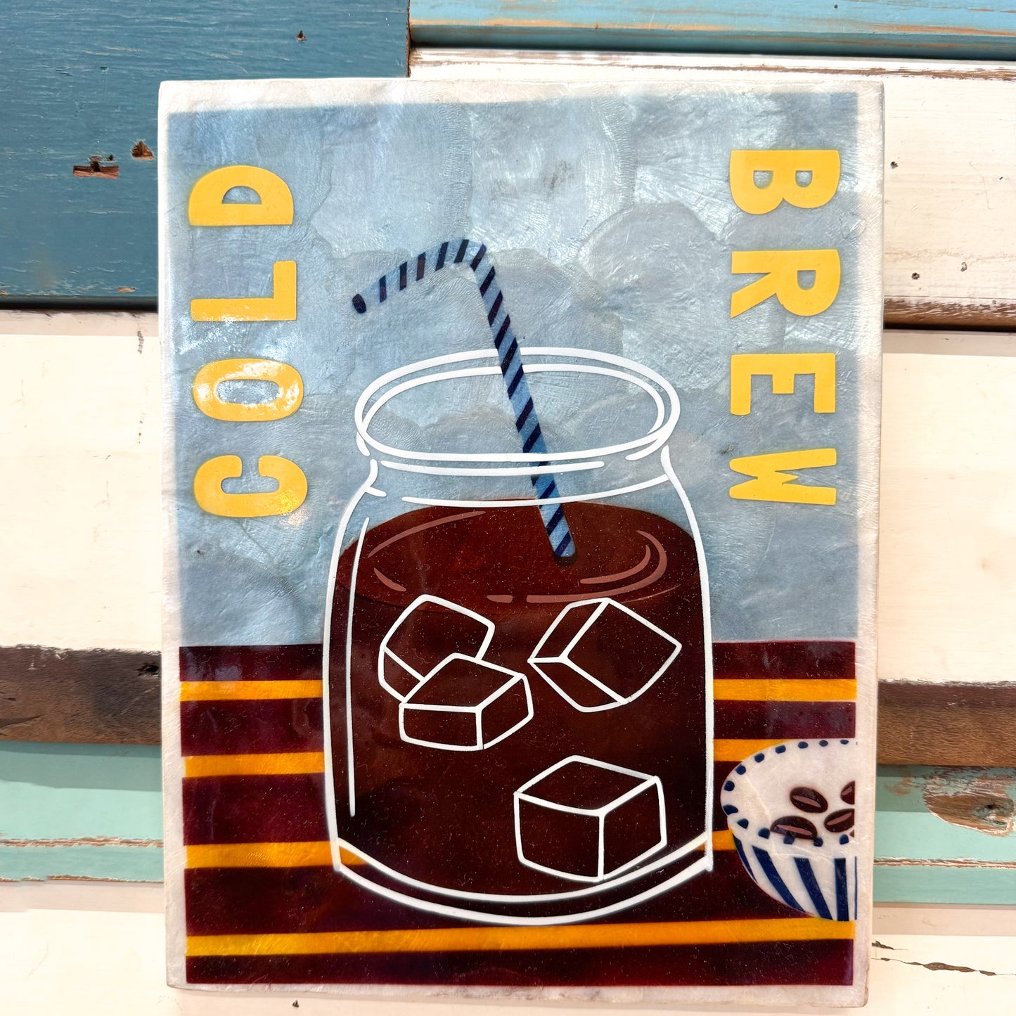 Capiz shell tile with a design of iced coffee in a mason jar, labeled 'Cold Brew', on a blue and red striped background.