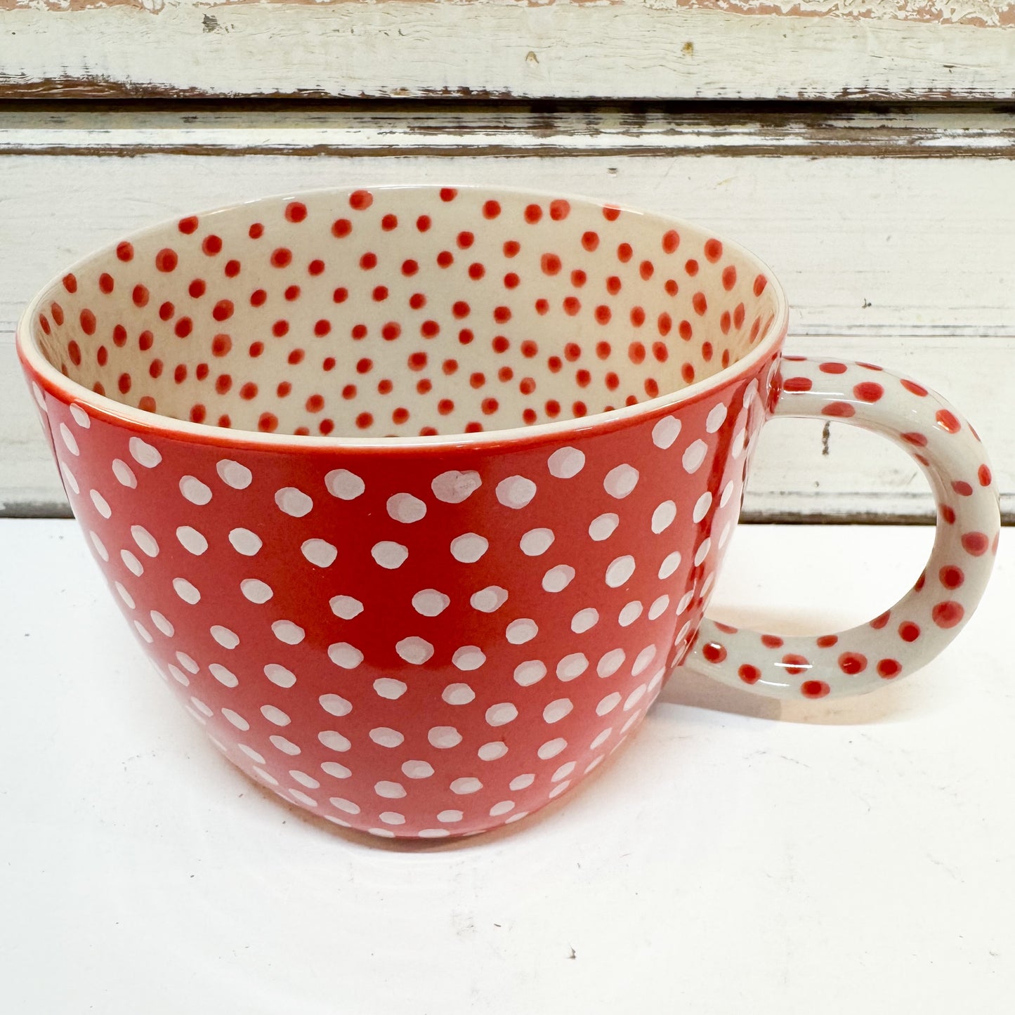 Jones & Co | Chino Mug - Red Spot 
A ceramic mug with a red and white polka dot pattern, shown from a front angle against a rustic white wooden background.