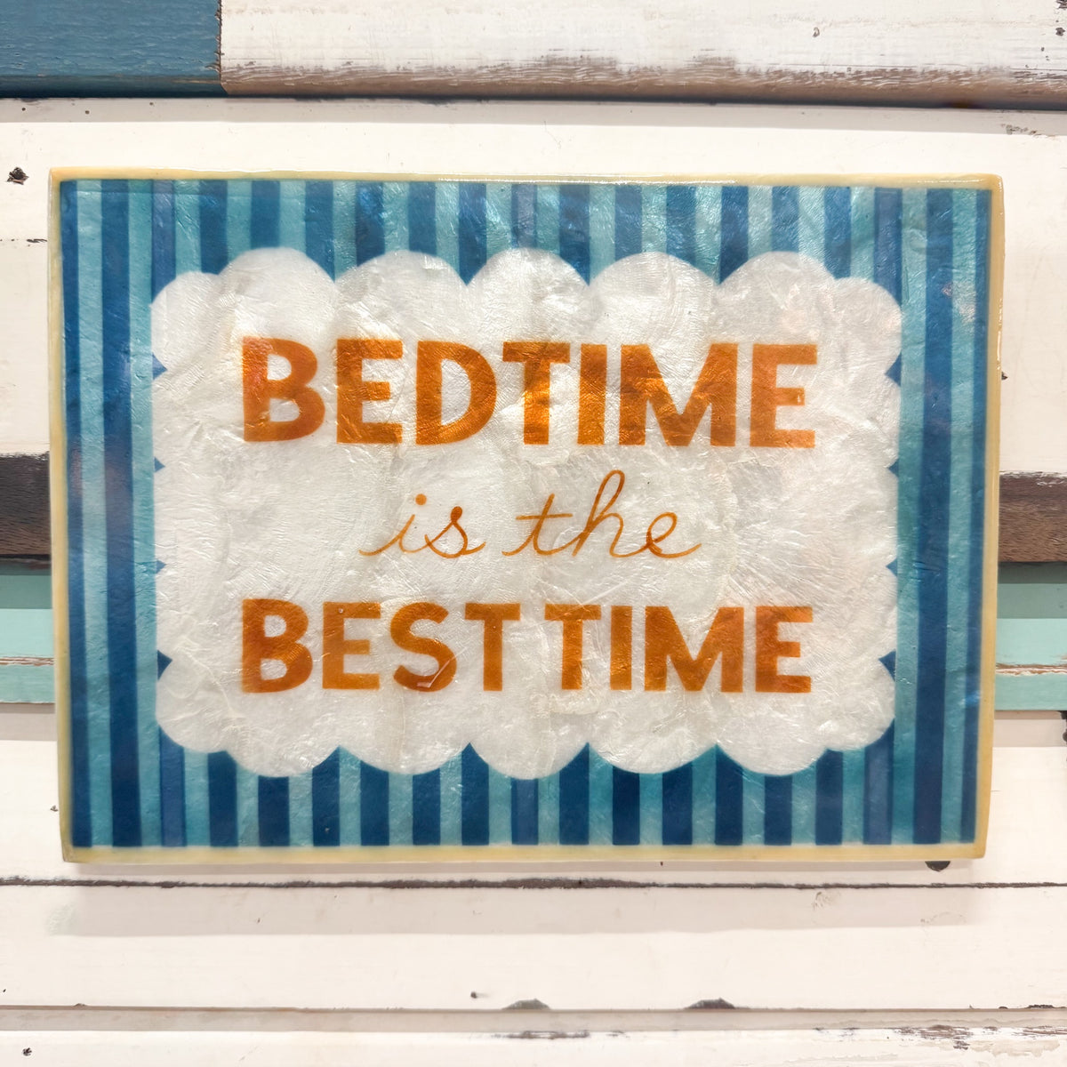 A square decorative wall sign with the phrase “BEDTIME is the BEST TIME” in orange lettering, mounted against a distressed white and blue wooden background.