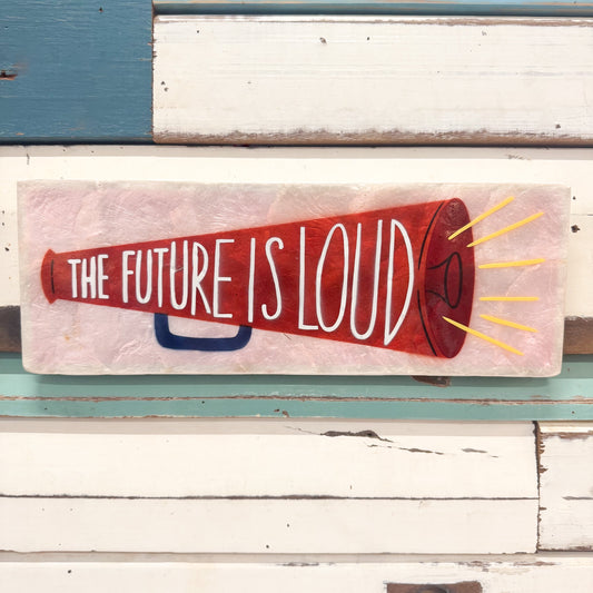 A rectangular painted sign featuring a red megaphone illustration with the phrase “THE FUTURE IS LOUD” in white lettering, mounted against distressed white and teal wood planks.
