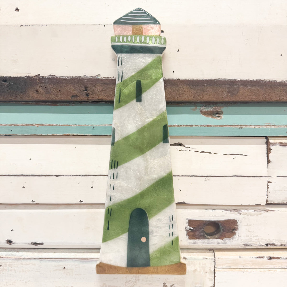 Hand-painted wooden lighthouse wall decor with green and white diagonal stripes, a dark green door, and a striped roof, shown against a rustic white wooden plank background.