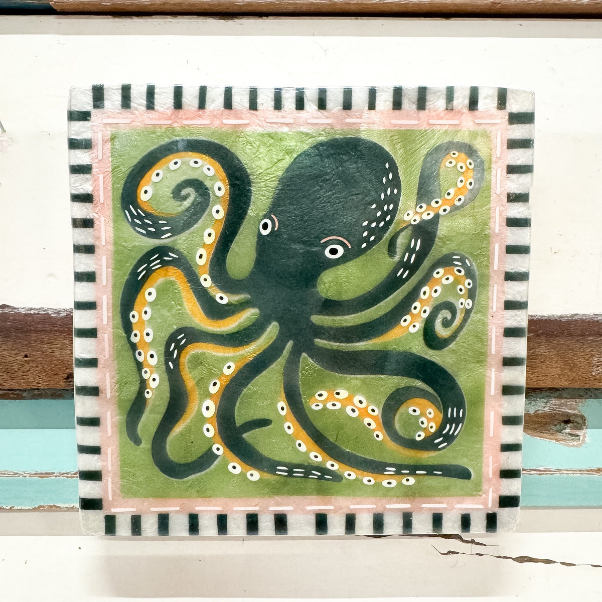 A square decorative tile or coaster featuring a hand-painted octopus design. The octopus is dark green with yellow and white tentacles and suckers, set against a light green background.