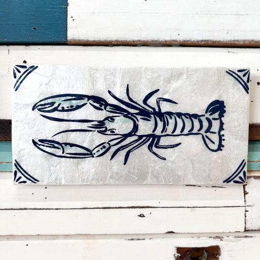 A rectangular decorative sign featuring a navy blue lobster illustration on a textured off-white background, mounted against a white wooden surface with teal and white painted boards.
Jones & Co | Taverna Lobster