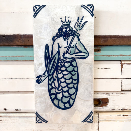 A vertical rectangular wall art print or tile featuring a stylized merman king with a crown, beard, trident, and shield in dark blue line art on a textured off-white background, displayed against a rustic white wood plank wall.
Jones & Co | Taverna Trident