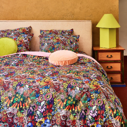Kip&Co - Paradise Organic Cotton Quilt Cover - multi coloured bright floral on black background fitted sheetBedroom with a colorful floral bedspread, matching pillows, and a wooden nightstand with a green lamp.
