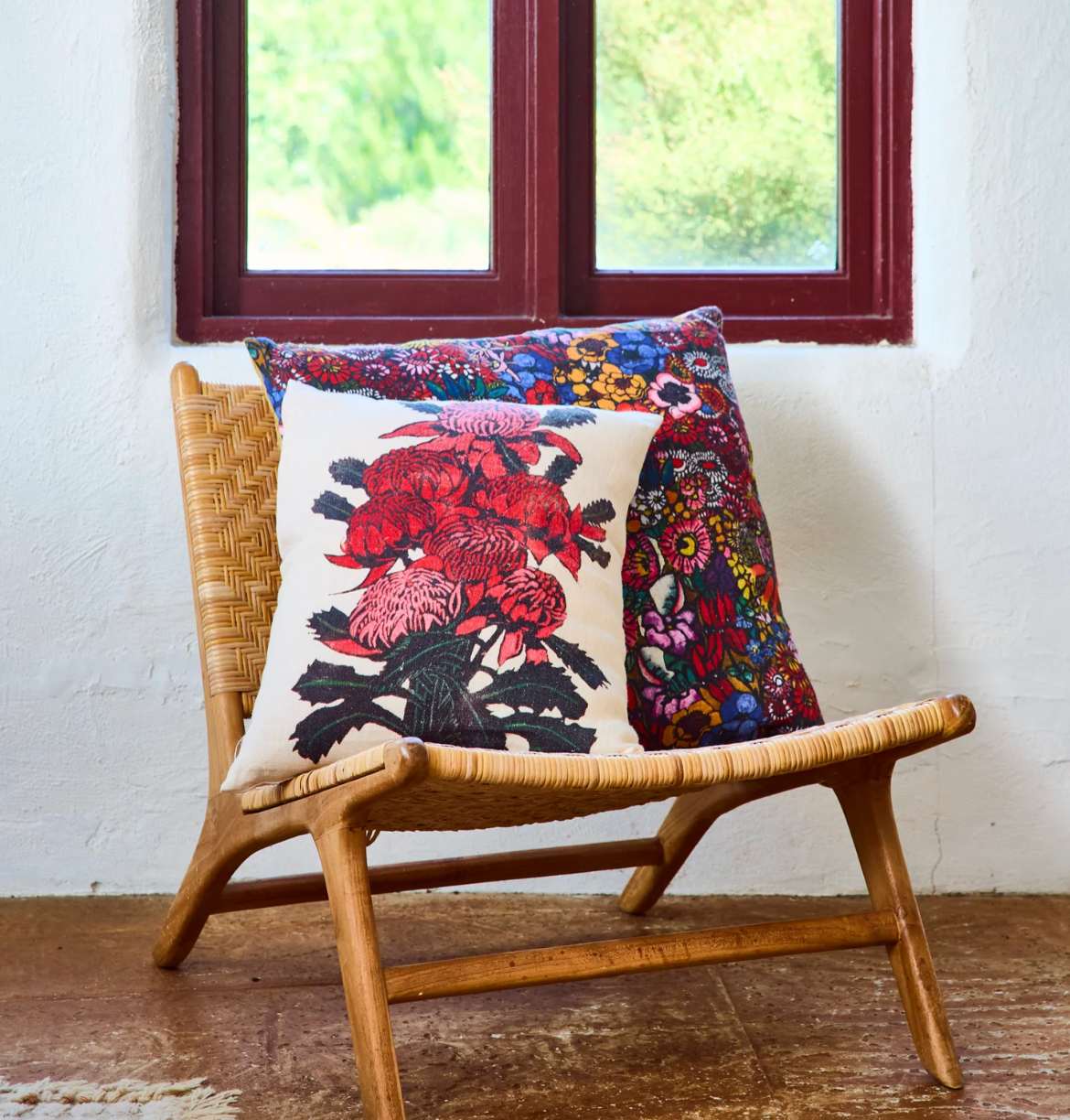 Decorative pillow with floral red Waratah design on a wicker chair in front of a window.