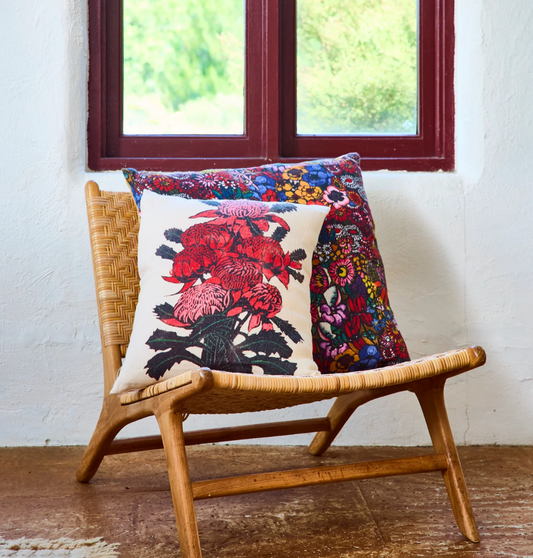 Decorative pillow with floral red Waratah design on a wicker chair in front of a window.