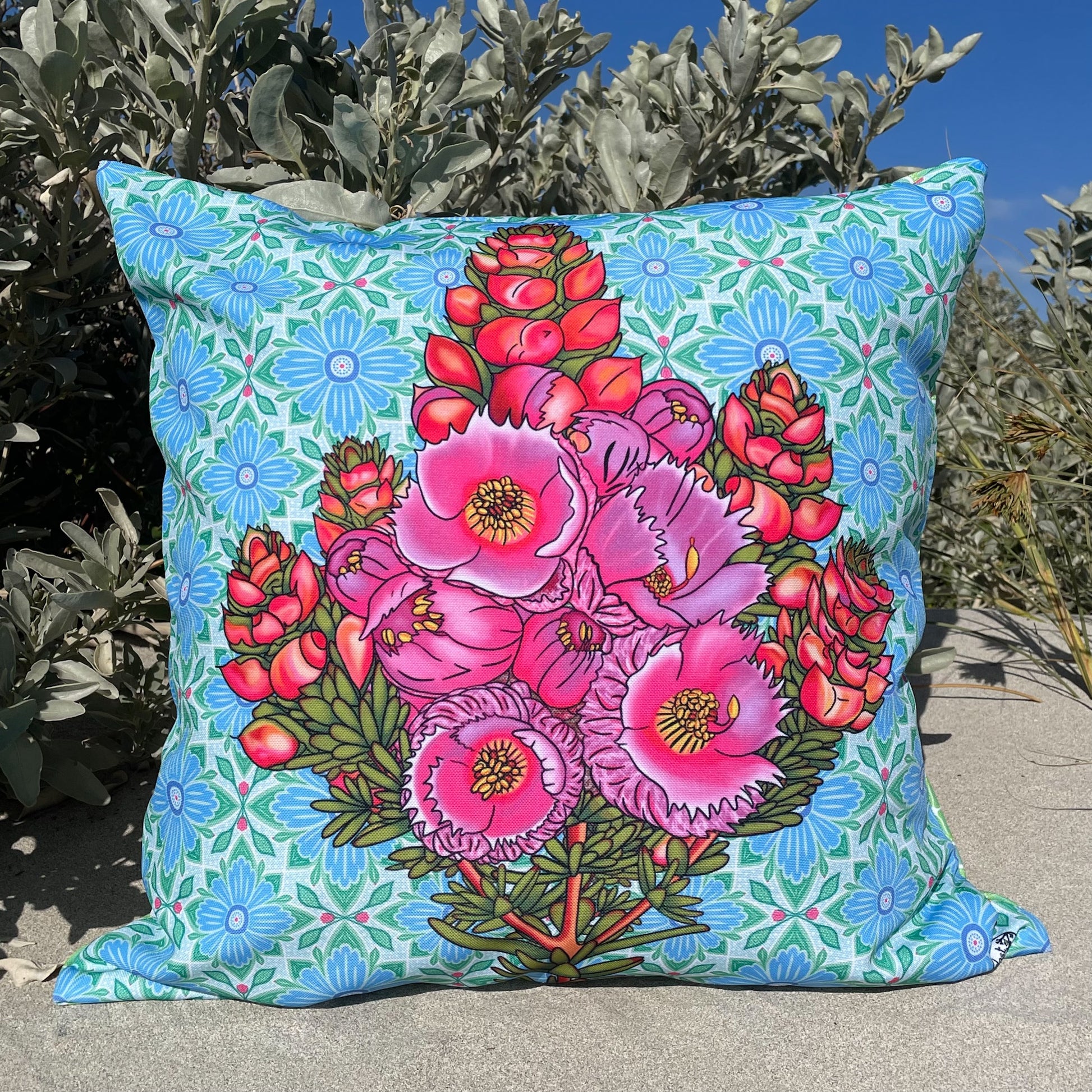 LOST AND FOUND ART CO Featherflower 60cm Cushion Decorative pillow with pink floral design on a blue floral background, placed outdoors.