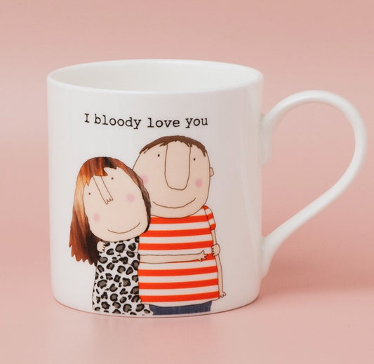 A white ceramic mug with a handle, featuring a cartoon illustration of a couple hugging and the text 'I bloody love you' printed above them, set against a solid pink background.