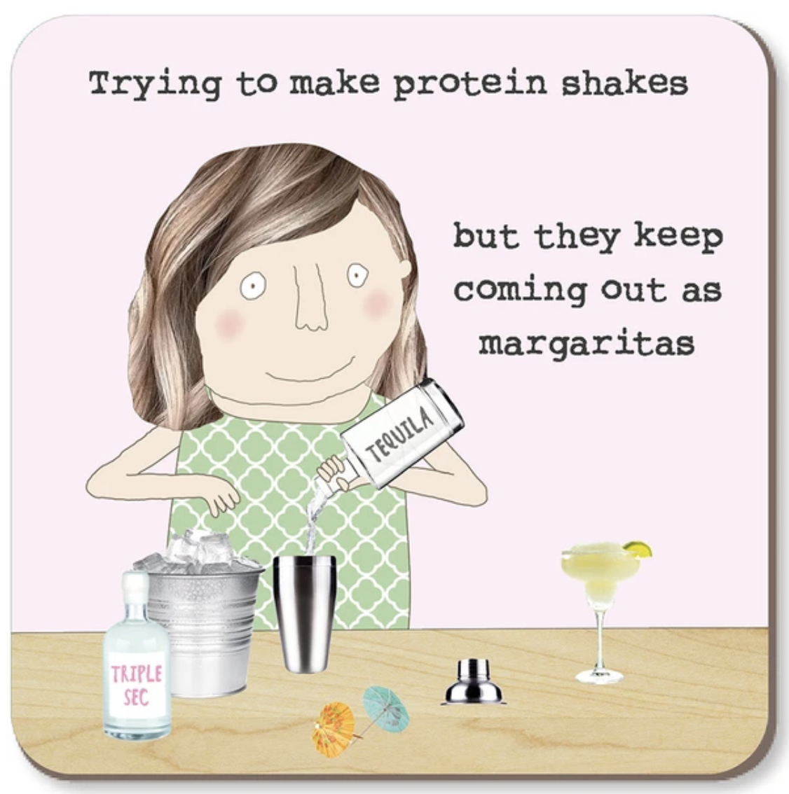 Square coaster featuring a cartoon illustration of a woman mixing a drink with the text 'Trying to make protein shakes but they keep coming out as margaritas'. The scene includes a shaker, ice bucket, tequila bottle, and margarita glass on a light wood surface against a pale pink background.