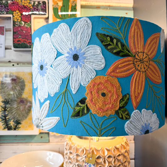 Floral embroidery on a blue background with a blurred background of more floral designs. Ruby Star | Daisy Drum Shade