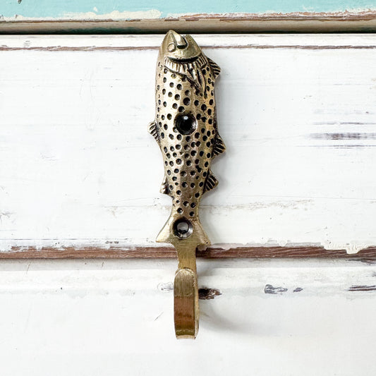 Brass fish-shaped hook on a white wooden surface