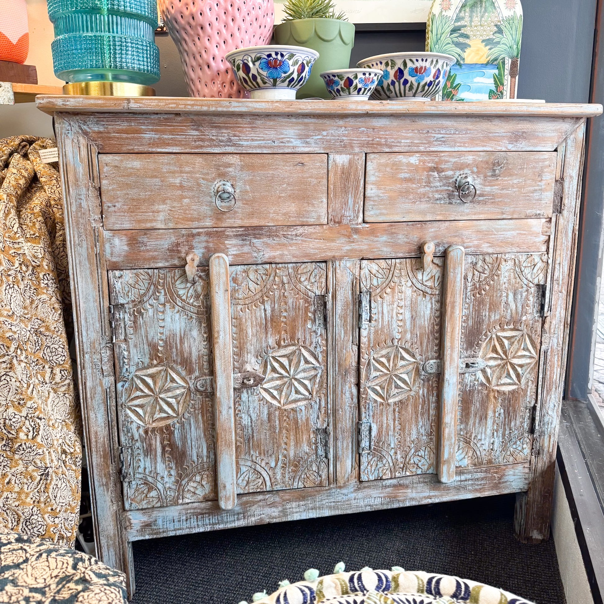 The Brightside Store - Antique Indian Teak Blue Wash Sideboard. Wooden cabinet with decorative carvings on a surface with decorative items around.