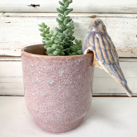 Pink ceramic planter with perched bird decoration attached to rim.