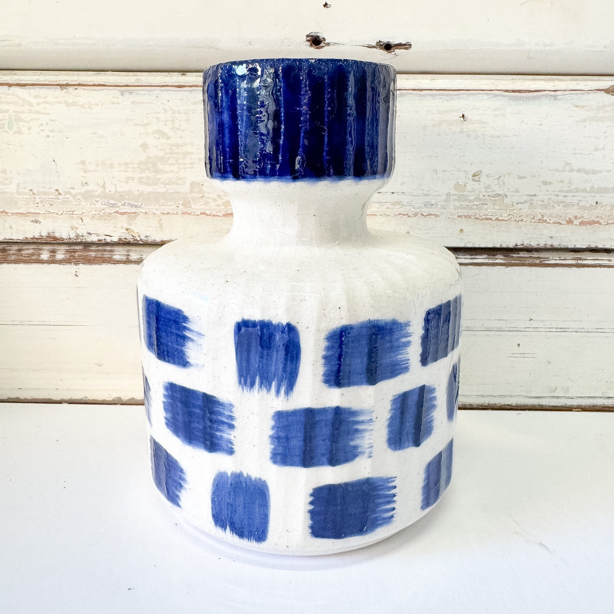 A handmade ceramic vase with a white body decorated with blue painted blocks, featuring a matching blue ribbed neck and lid. The Brightside Store | Blue Romane Vase - Medium