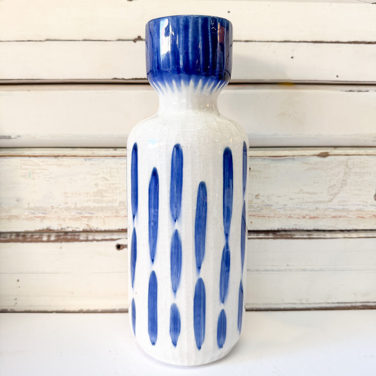 A white ceramic bottle with a glossy blue ribbed neck and lid, decorated with vertical blue oval patterns on the body. The Brightside Store | Blue Romane Vase - Tall