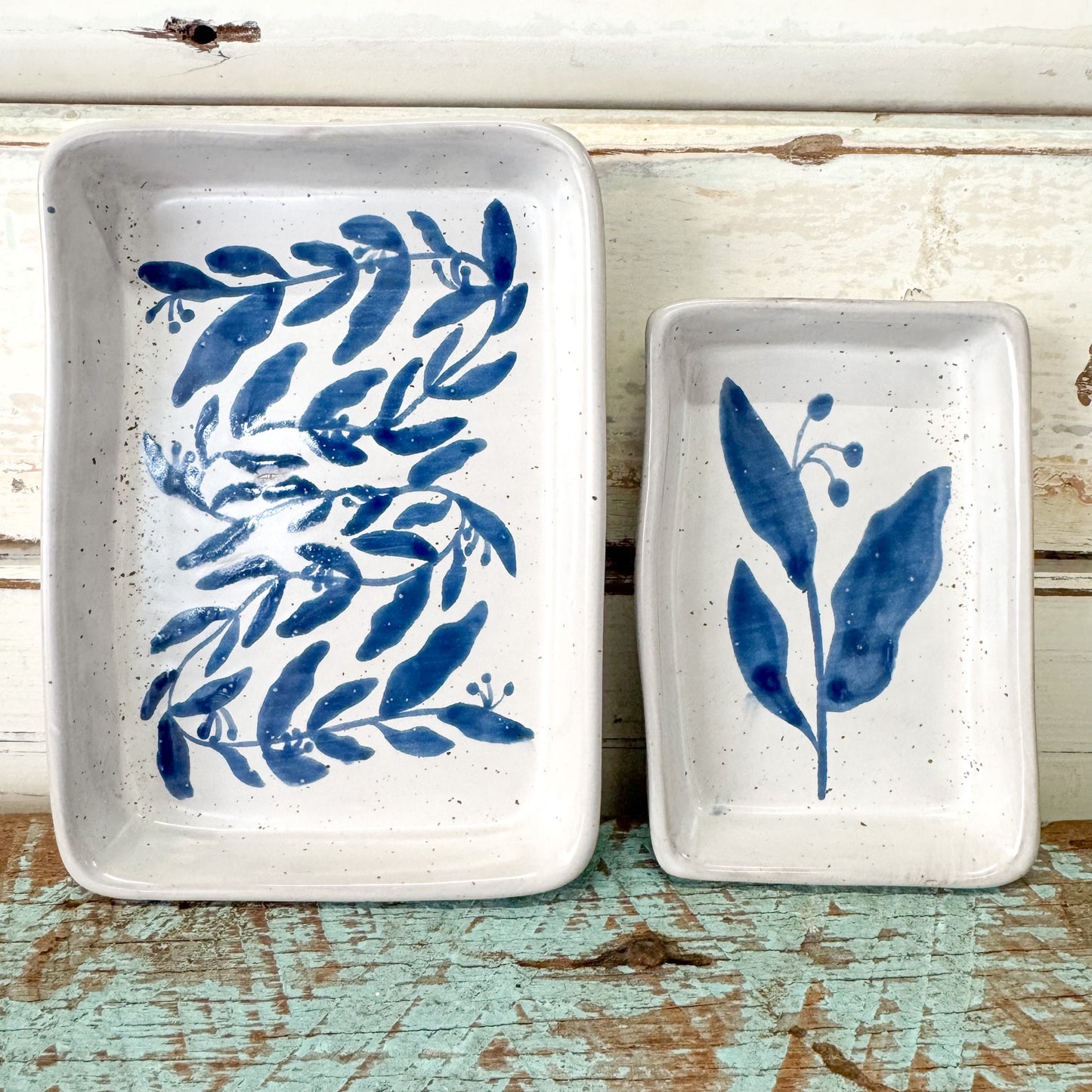 Two ceramic trays with blue leaf patterns on a rustic wooden surface.