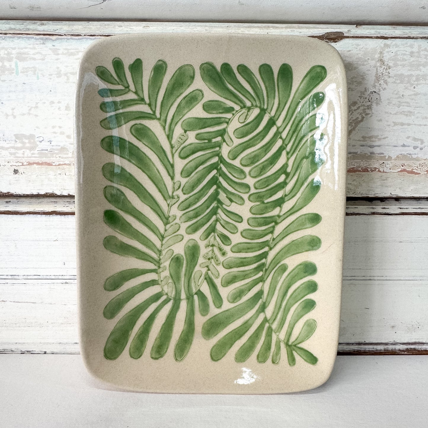 Ceramic tray with green leaf pattern on a wooden surface