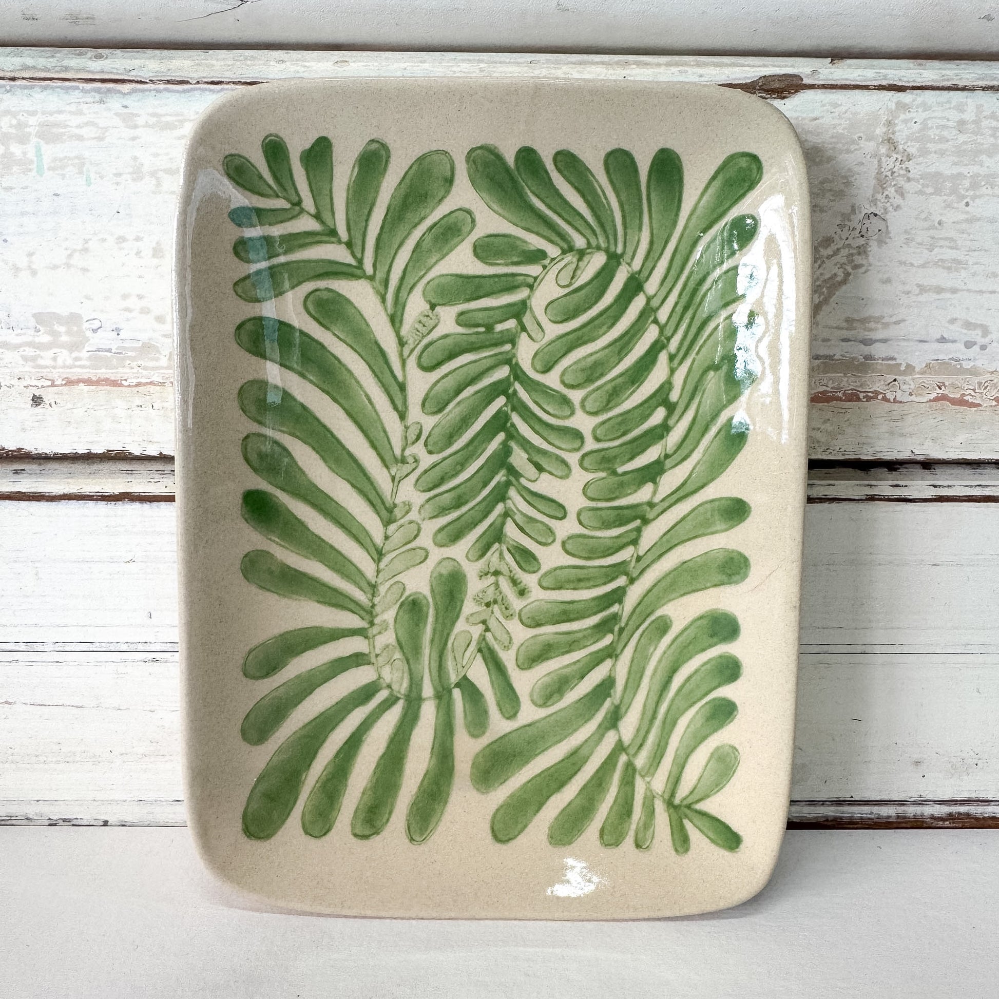 Ceramic tray with green leaf pattern on a wooden surface