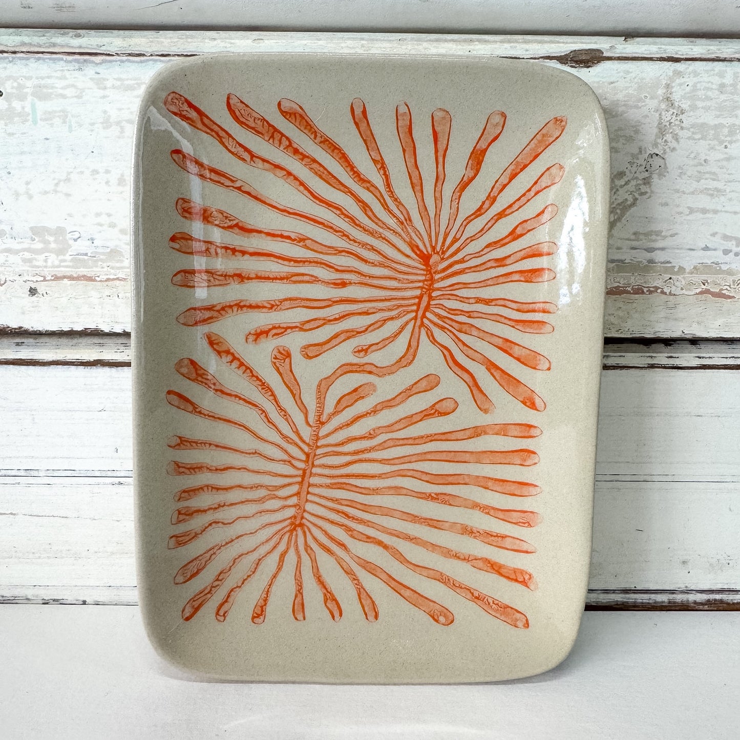 Rectangular ceramic plate with orange fan coral pattern on a white wooden background