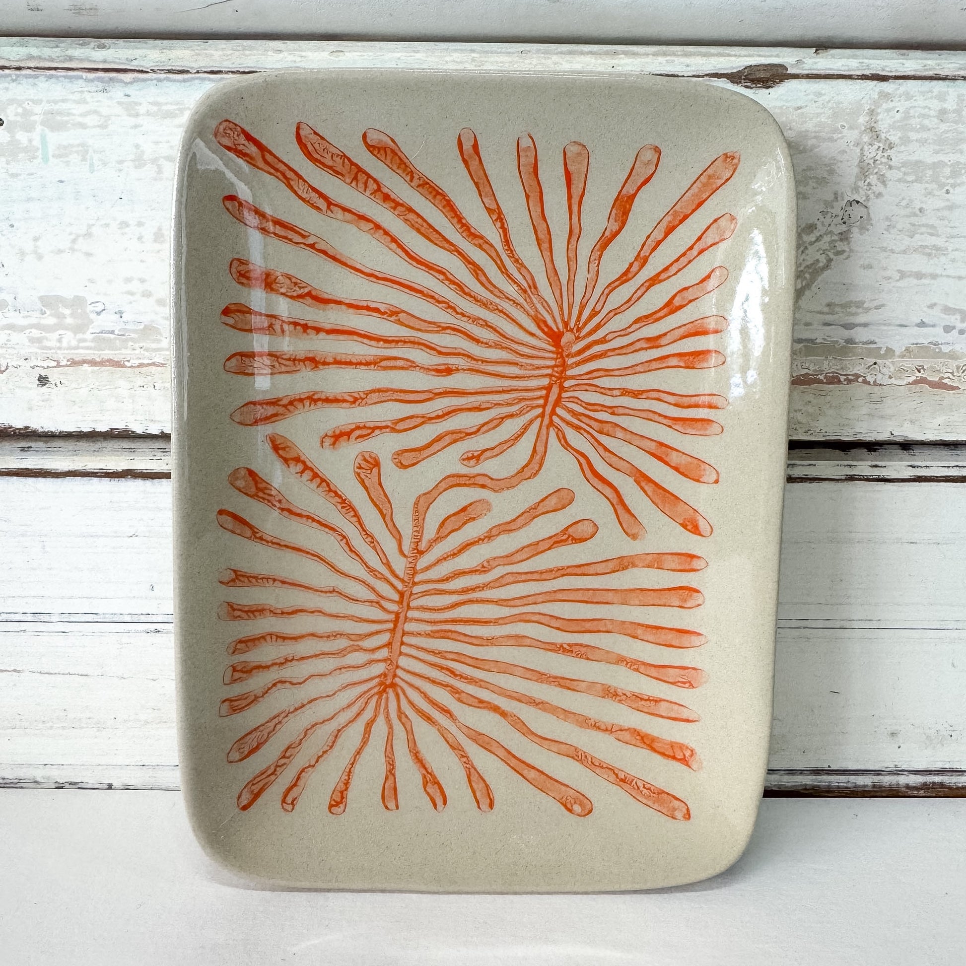 Rectangular ceramic plate with orange fan coral pattern on a white wooden background