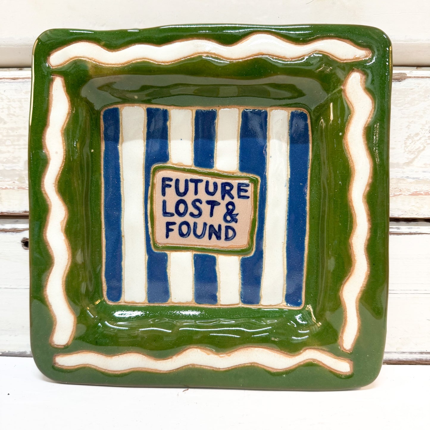 The Brightside Store | Lingo Tray - Lost and Found A square ceramic dish with a green glazed border, cream wavy accents, and blue-and-white vertical stripes in the center. A small cream label in the middle reads 'FUTURE LOST & FOUND' in blue lettering.