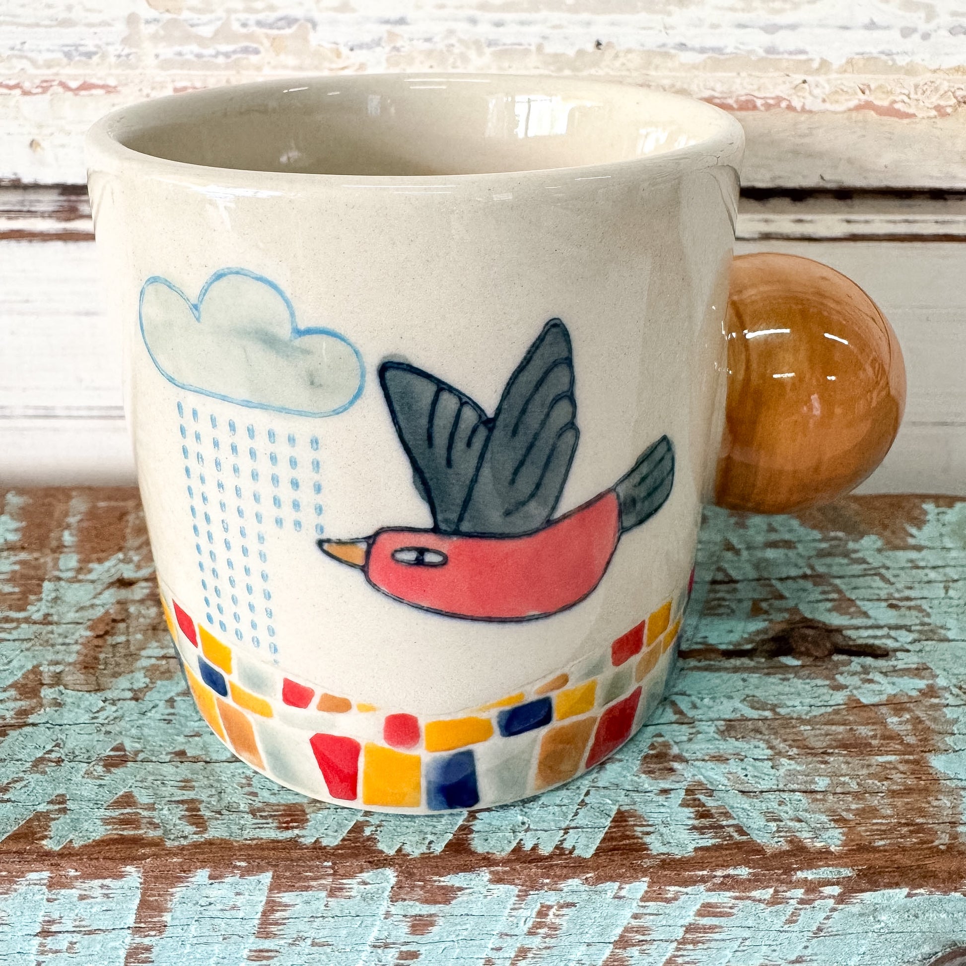 Ceramic mug with a bird and cloud design on a wooden surface