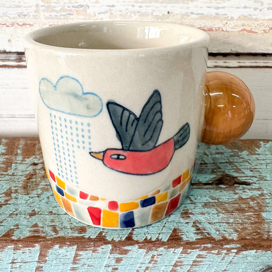 Ceramic mug with a bird and cloud design on a wooden surface