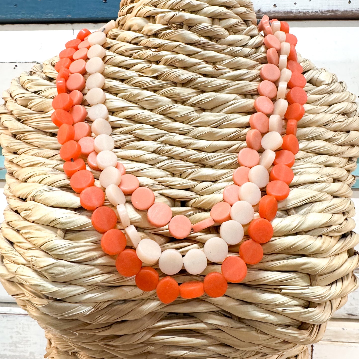 Three layered beaded necklaces with round disc beads in shades of orange, coral, and cream, displayed on a woven straw jewelry stand. The Brightside Store | Pop Necklace - Jaffa Orange